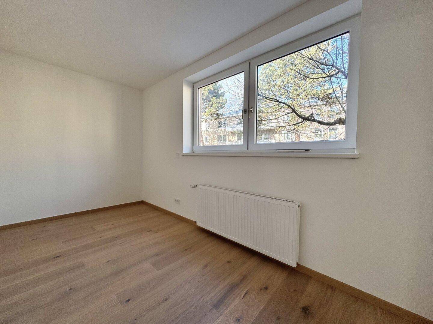 Heller Raum mit Fenster, Heizkörper und neuem Holzparkettboden, ideal für ein Schlafzimmer.
