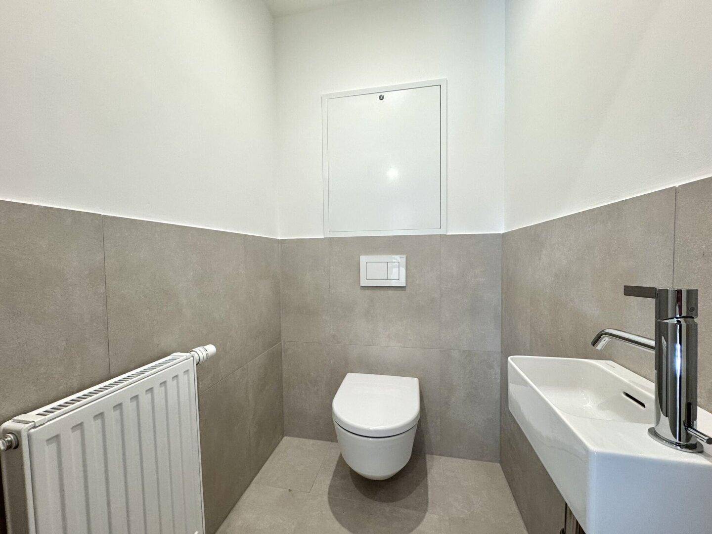 Modernes Gäste-WC mit Wand-WC, kleinem Waschbecken und grauen Fliesen, funktional und stilvoll.
