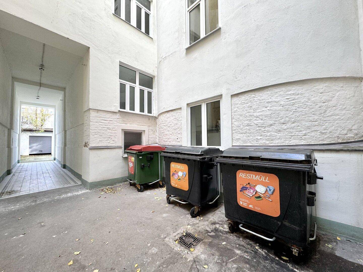 Innenhof des Gebäudes mit Mülltonnen und weiß gestrichenen Fassaden.
