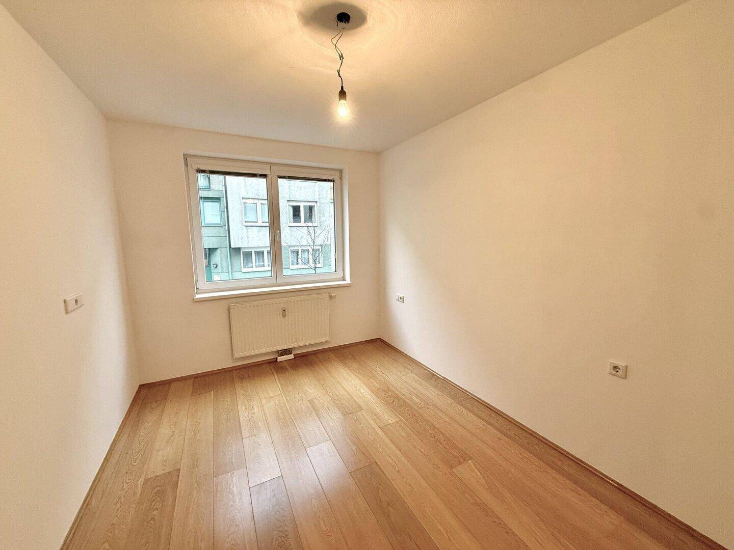 Heller, leerer Raum mit Parkettboden und Fenster, ideal für Schlafzimmer oder Büro.