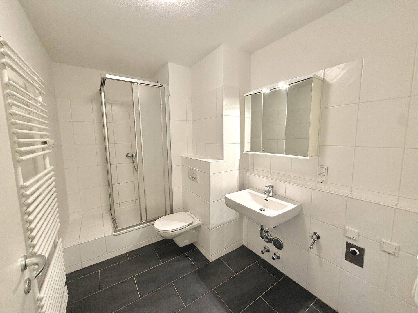 Modernes Badezimmer mit Dusche, WC, Waschbecken und beheiztem Handtuchhalter.