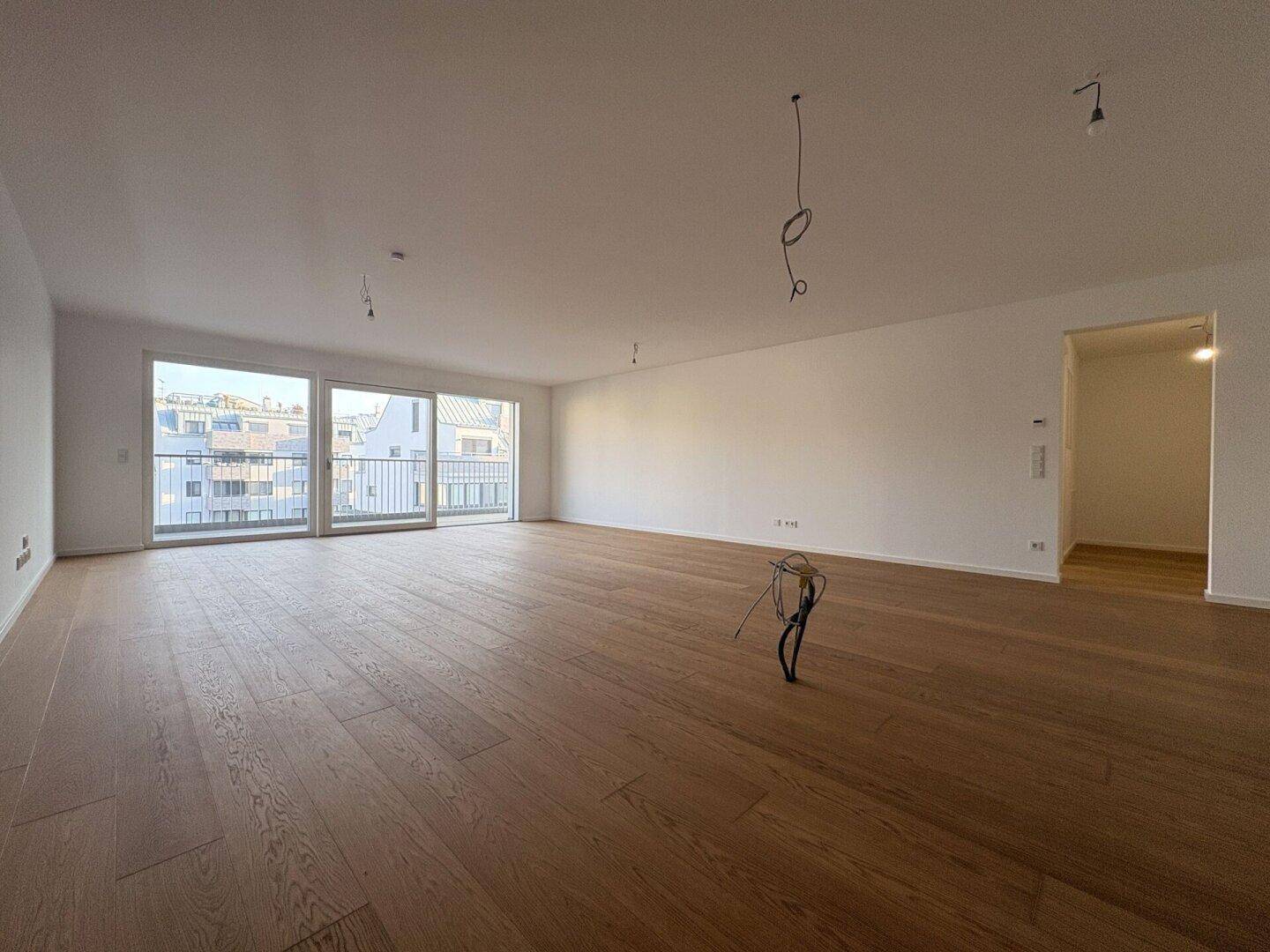 Heller, leerer Wohnraum mit Holzboden und Zugang zu einem französischen Balkon.
