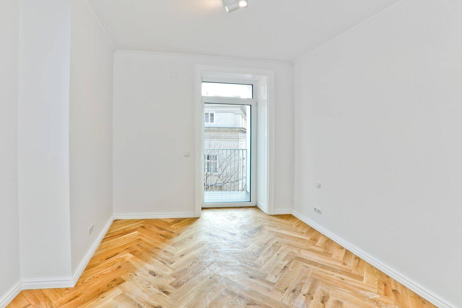 Heller Raum mit Fischgrätparkett und Zugang zu einem charmanten französischen Balkon.