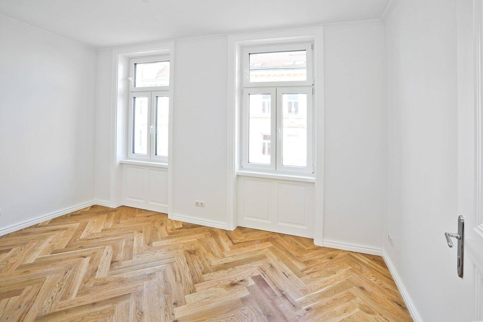 Geräumiger, heller Raum mit Fischgrätparkett und hohen Fenstern, bereit zum Einzug.