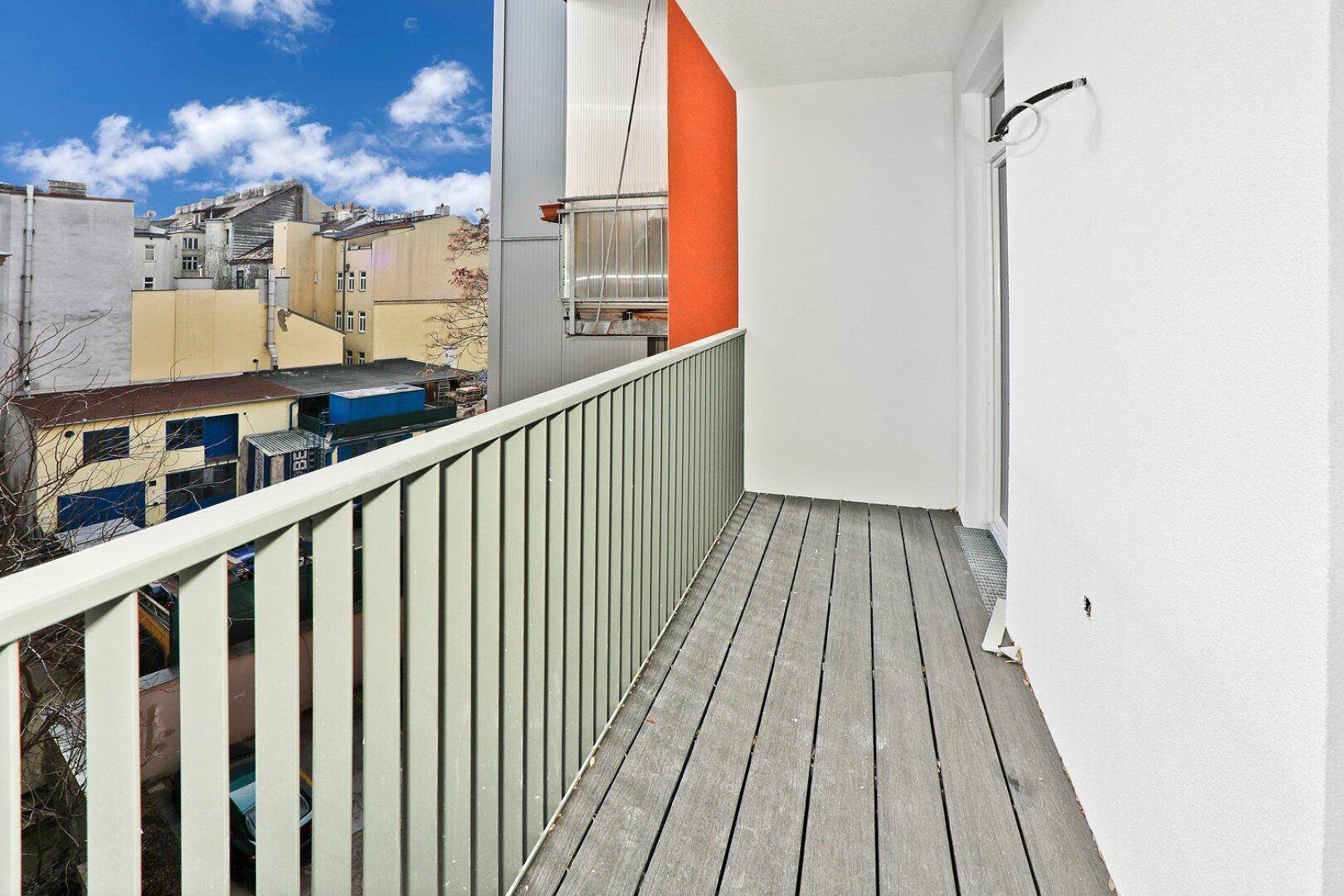 Geräumiger Balkon mit modernen Holzdielen und Blick auf die umliegenden Gebäude.