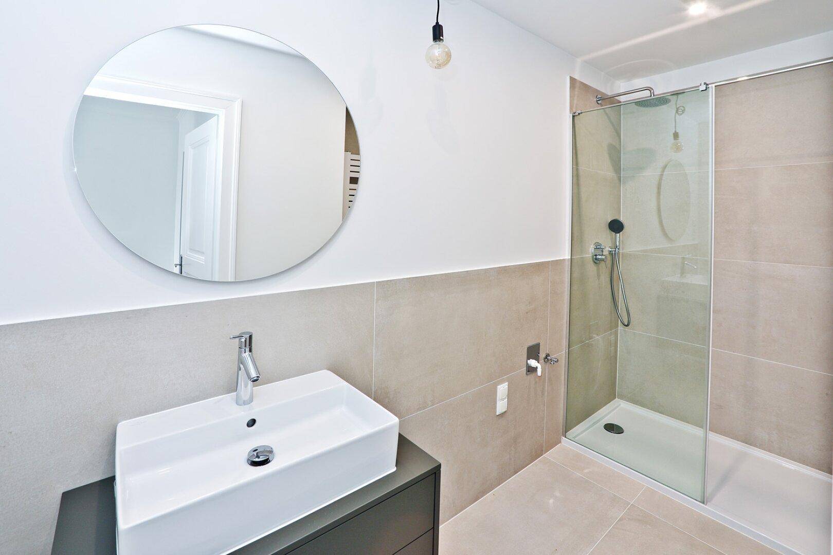 Modernes Badezimmer mit begehbarer Dusche, Einzelwaschbecken und großem Rundspiegel.