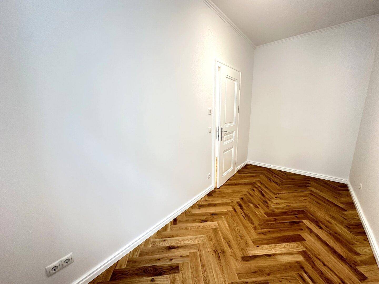Geräumiges Zimmer mit Fischgrätparkett und weißer Tür, ideal für individuelle Gestaltung.