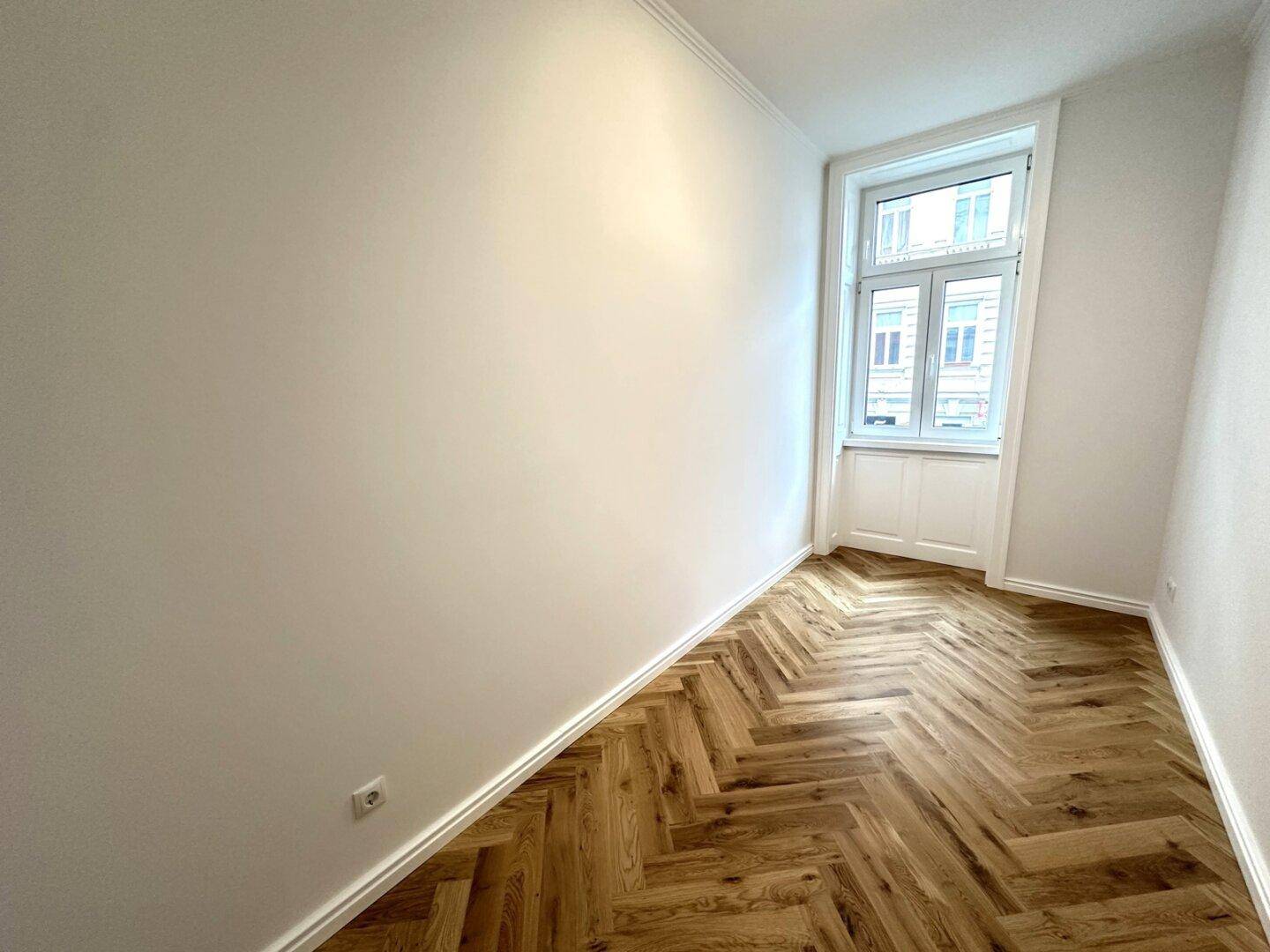 Renoviertes Zimmer mit Fischgrätparkett und weißer Wandgestaltung, bereit zum Einzug.