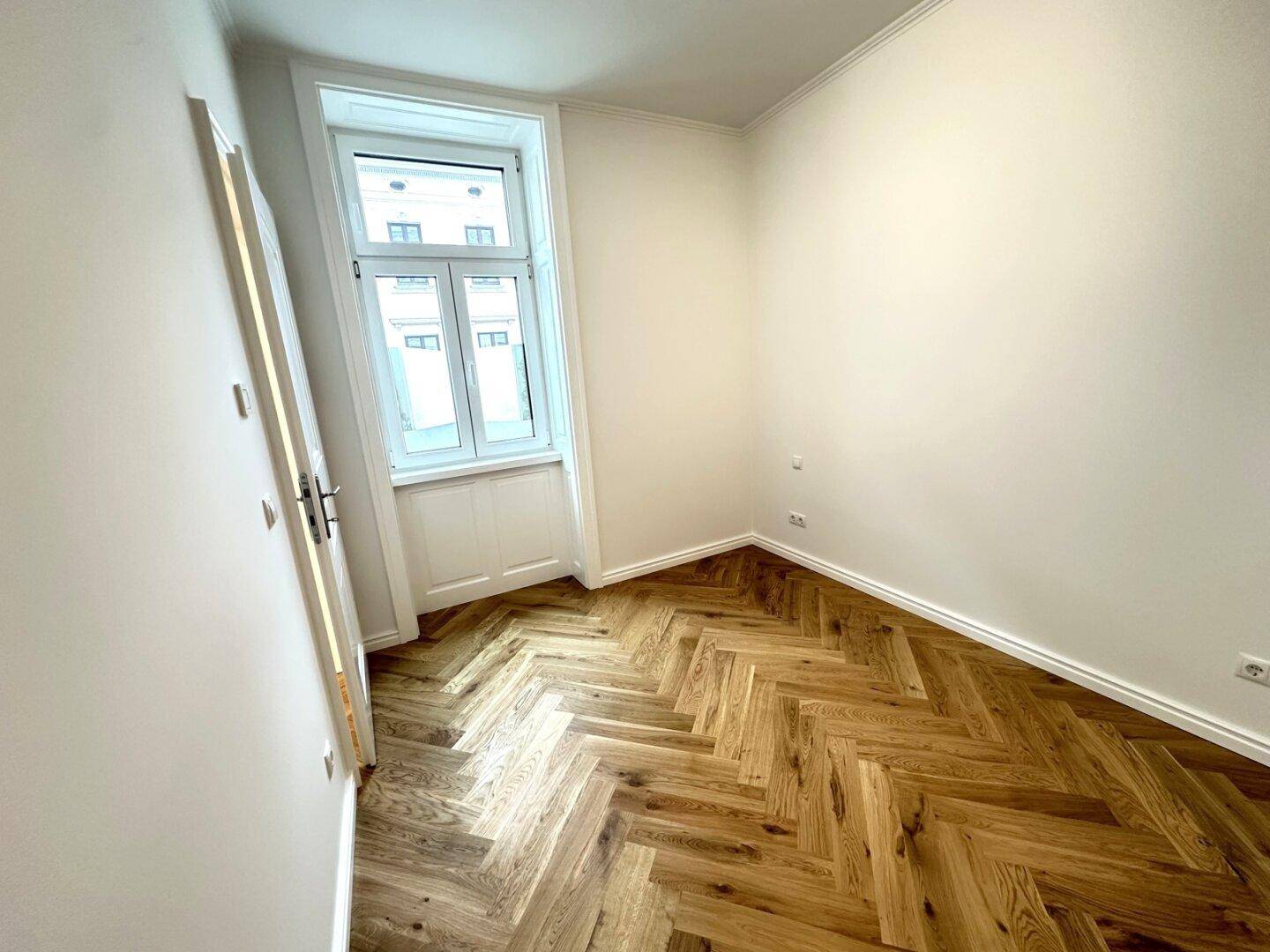 Gemütliches Zimmer mit Fischgrätparkett und einem großen Fenster, ideal als Schlaf- oder Arbeitszimmer.