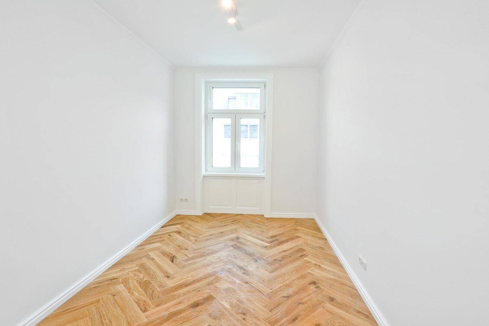Kleineres Zimmer mit Fischgrätparkett und einem Fenster, geeignet als Schlaf- oder Arbeitszimmer.