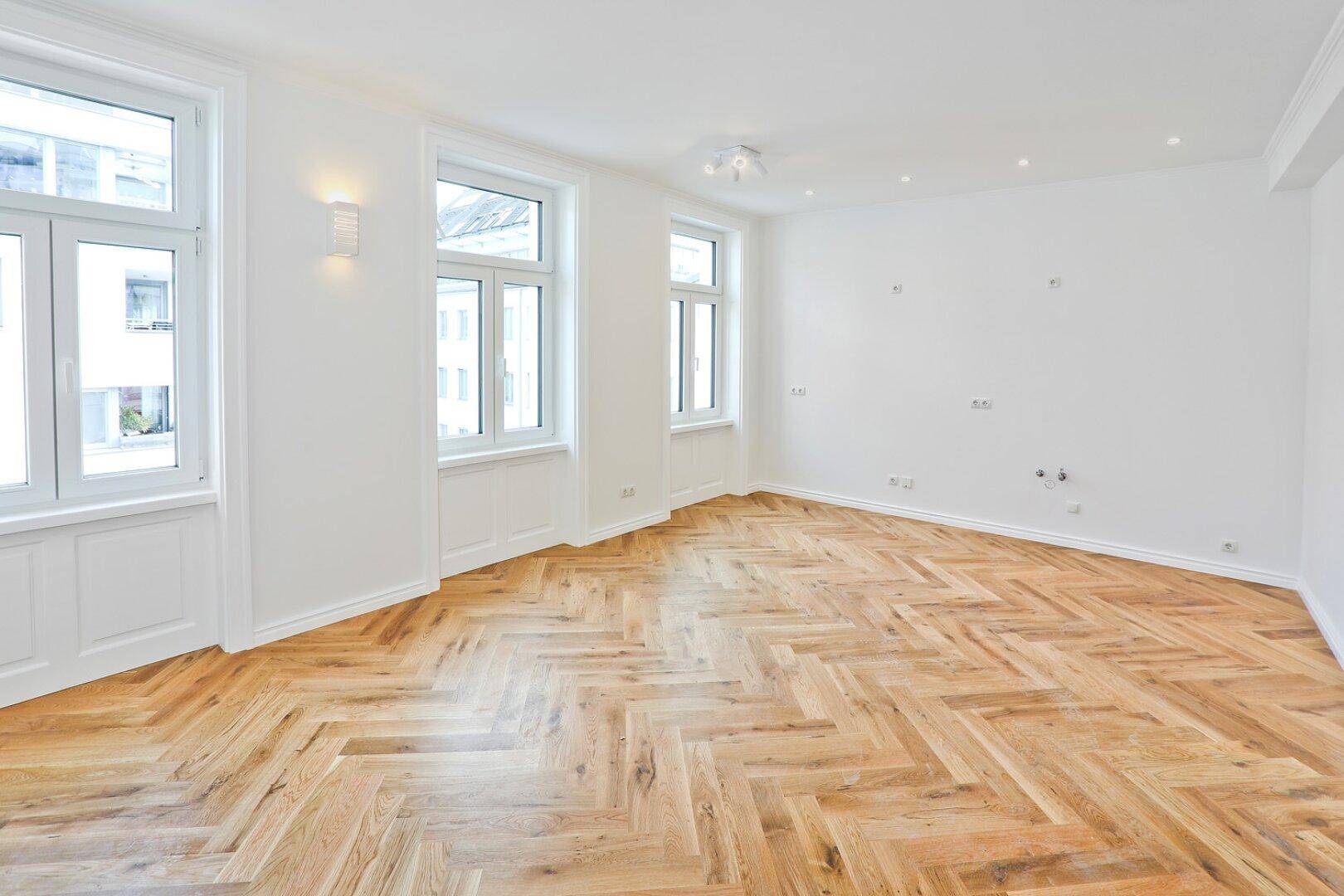 Geräumiges Zimmer mit Fischgrätparkett und großen Fenstern, ideal für einen Wohnbereich.