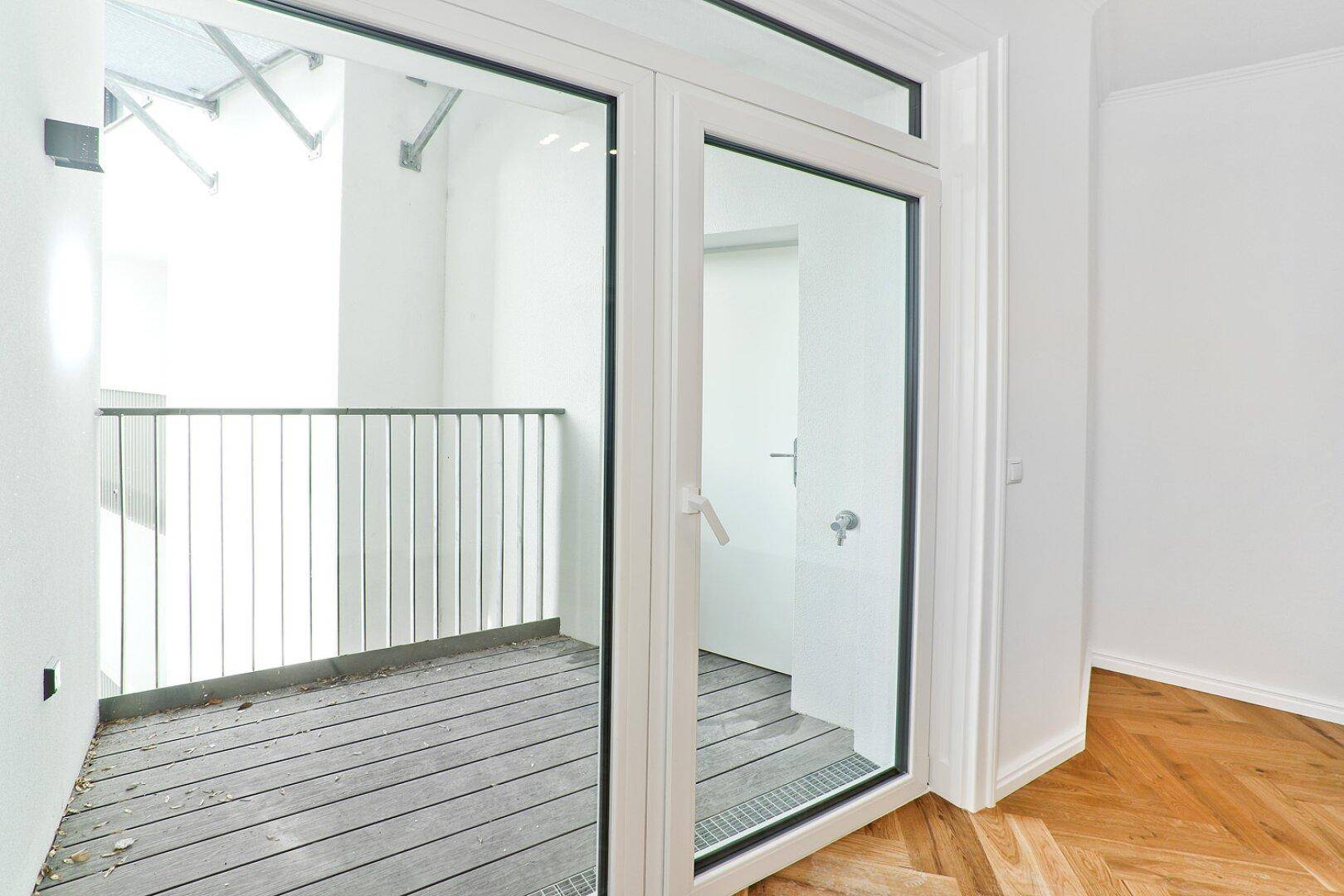 Glastür führt von einem Innenraum auf einen kleinen Balkon mit Holzbelag.