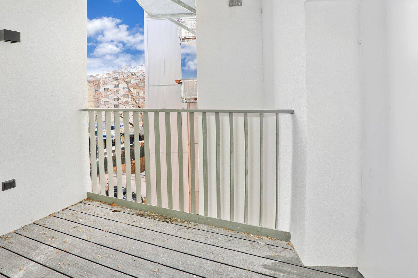 Kleiner Balkon mit Holzbelag und Metallgeländer, bietet einen Blick auf die Umgebung.