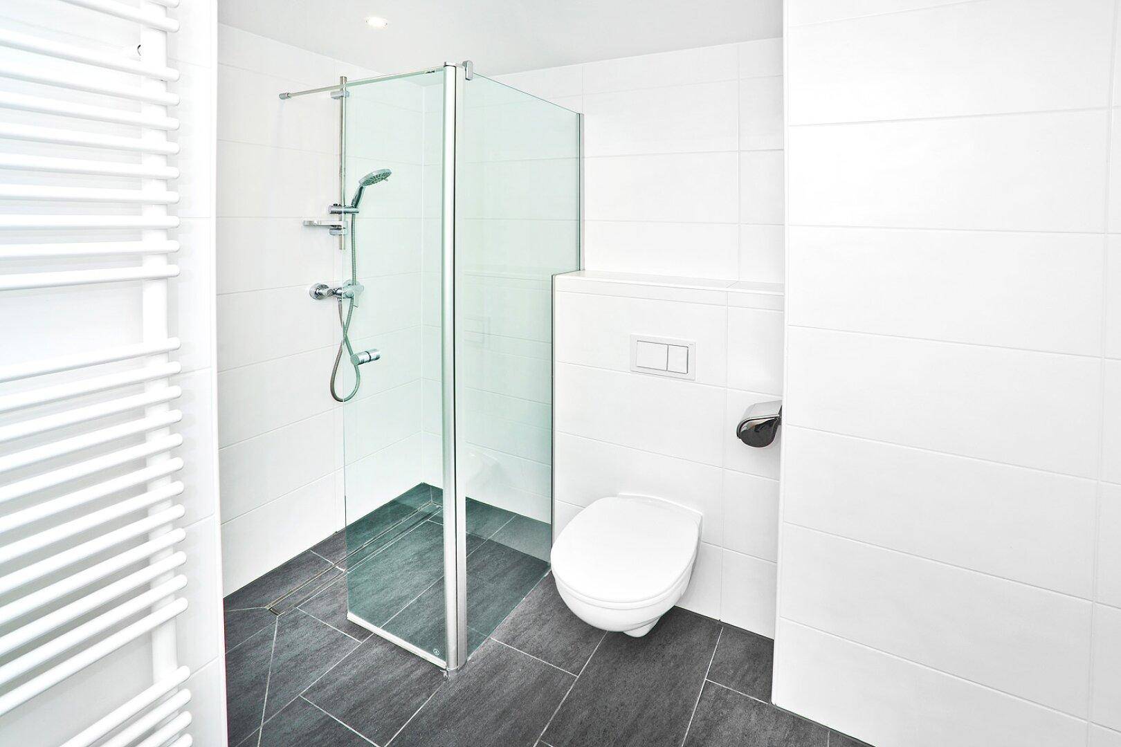 Modernes Badezimmer mit ebenerdiger Dusche, Wand-WC und praktischem Handtuchheizkörper.