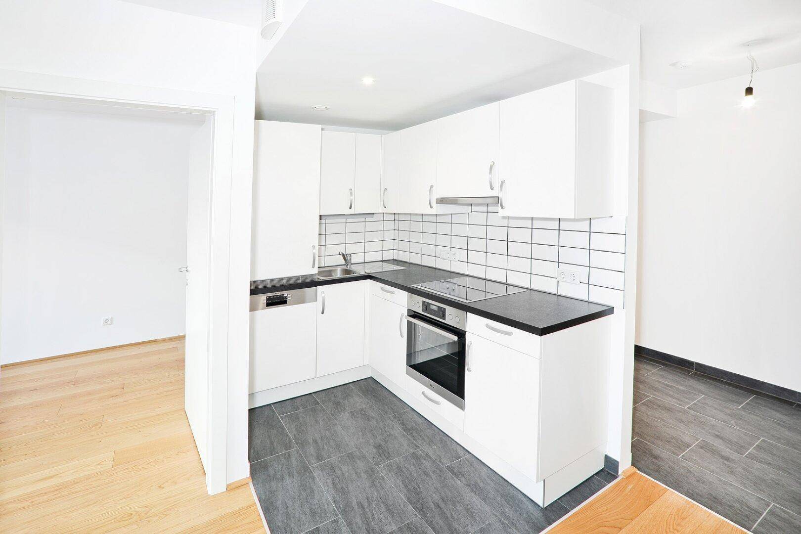 Helle Einbauküche mit modernen Geräten und Blick in den angrenzenden Wohnbereich.