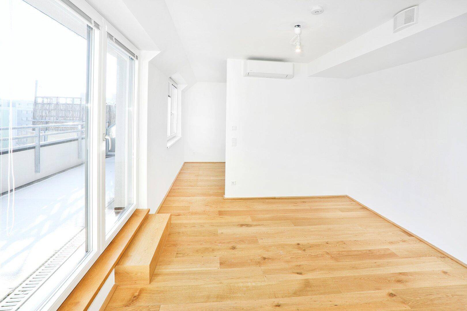 Heller, leerer Wohnbereich mit Holzboden und Zugang zu einem großen Balkon, ideal für offenes Wohnen.