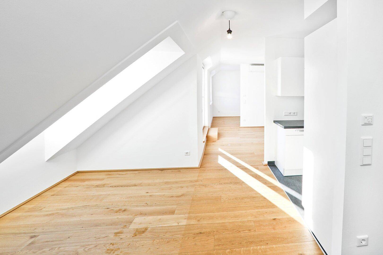 Lichtdurchfluteter Flurbereich mit Holzboden und Dachfenster, der zu einem Küchenbereich führt.