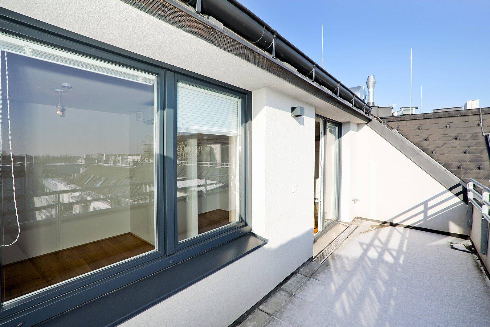 Sonniger Balkon mit Metallgeländer und Blick auf die Dächer der Stadt, angrenzend an den Wohnbereich.