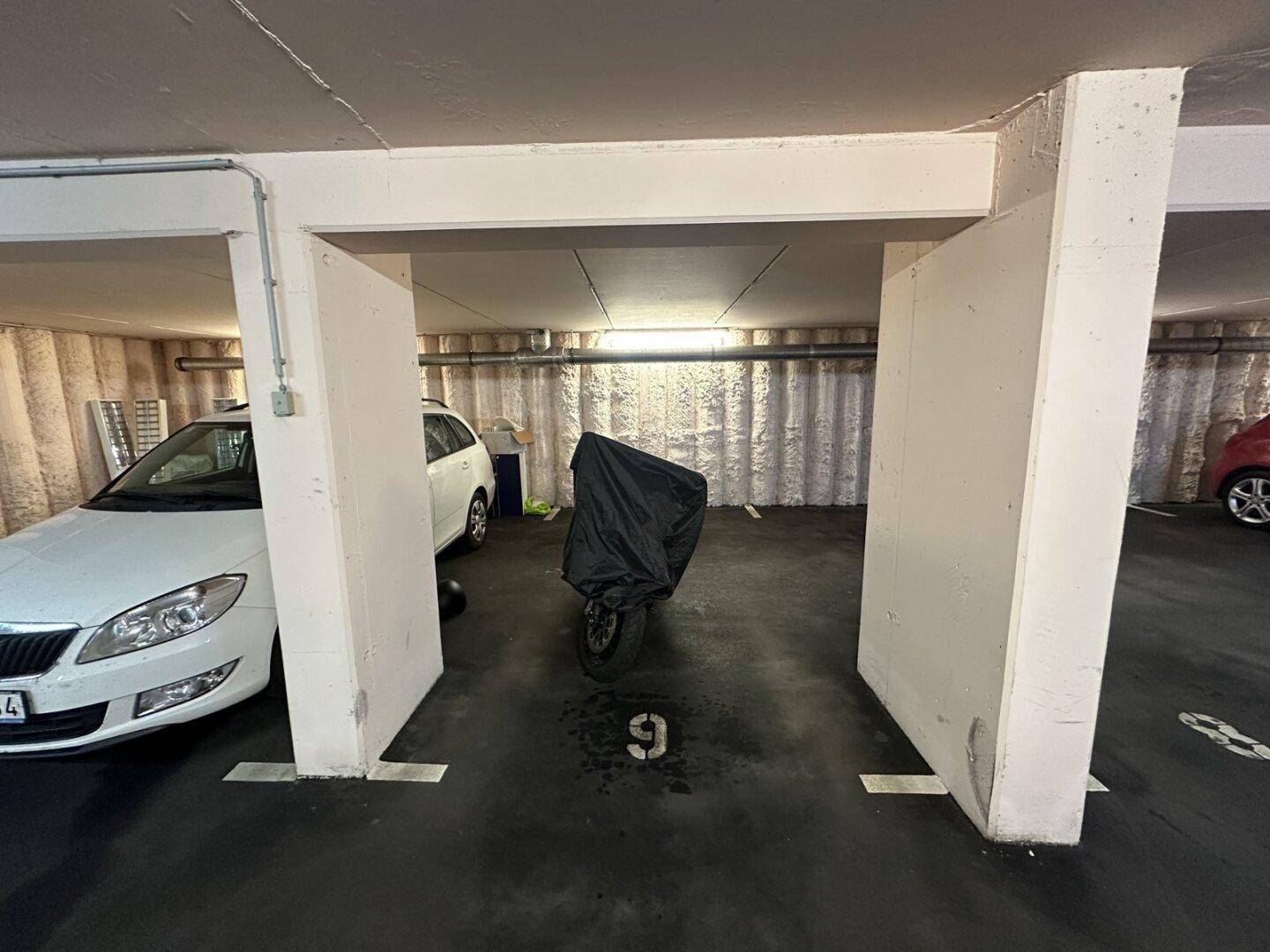 Tiefgarage mit markierten Stellplätzen und einem abgedeckten Motorrad, gut beleuchtet.