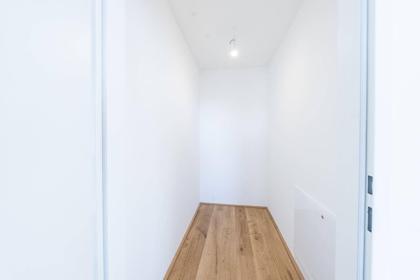 Leerer Abstellraum mit Holzboden und weißen Wänden, bereit zur individuellen Nutzung.