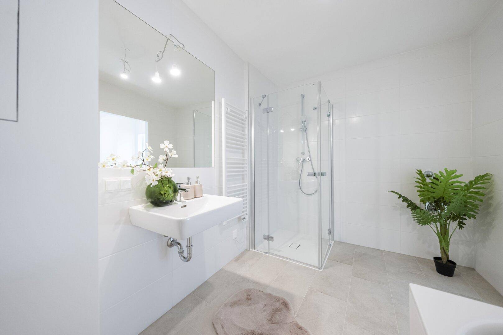 Modernes Badezimmer mit Duschkabine, Waschbecken und großem Spiegel, hell und funktional.