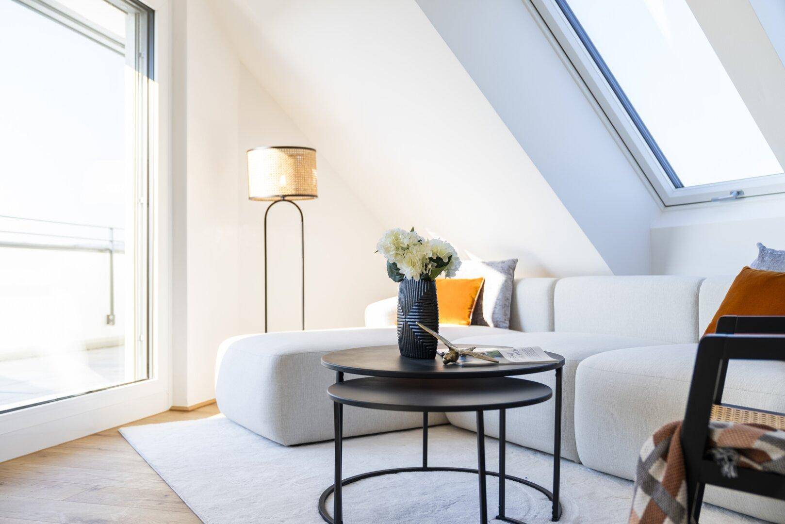 Heller Wohnbereich im Dachgeschoss mit Sofa, Beistelltischen und Zugang zum Balkon.
