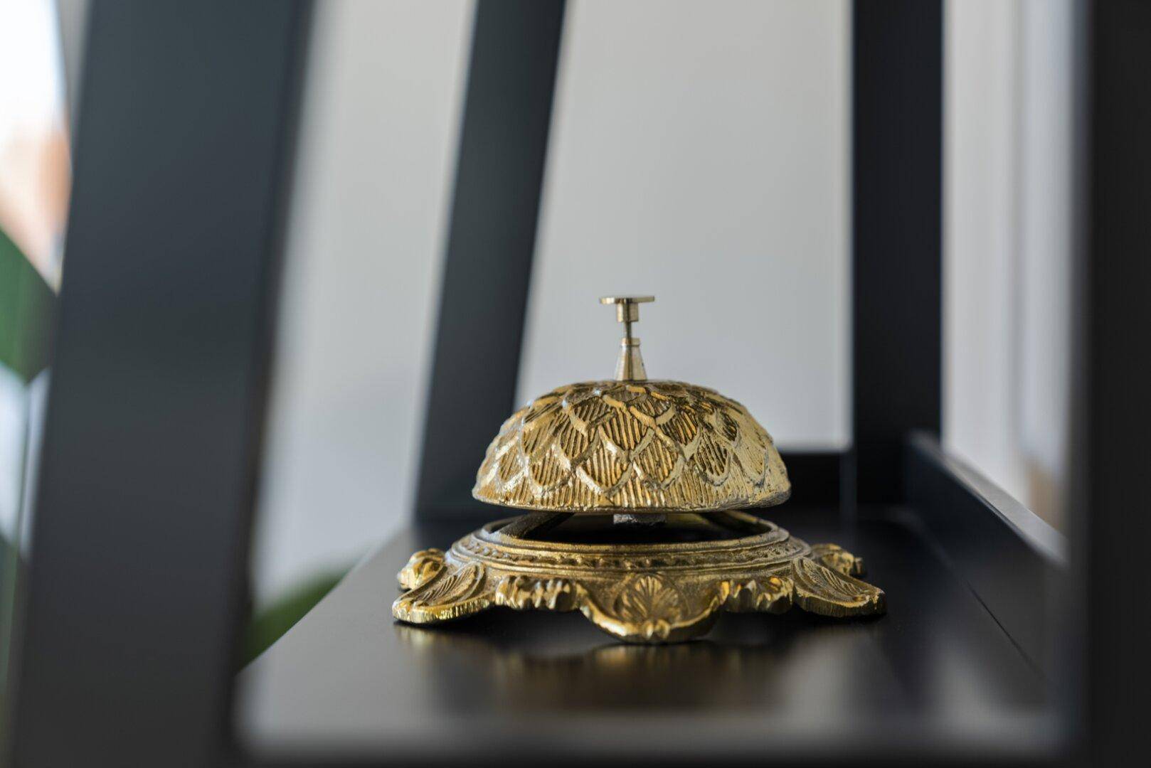 Eine goldene Rezeptionsglocke als dekoratives Element auf einem dunklen Regal.