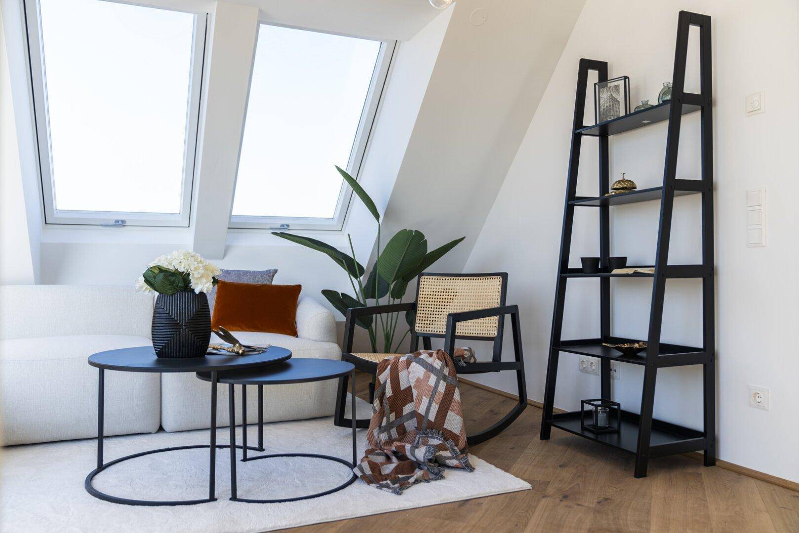 Heller Wohnbereich im Dachgeschoss mit Holzboden, Sofa, Beistelltischen und Regal.