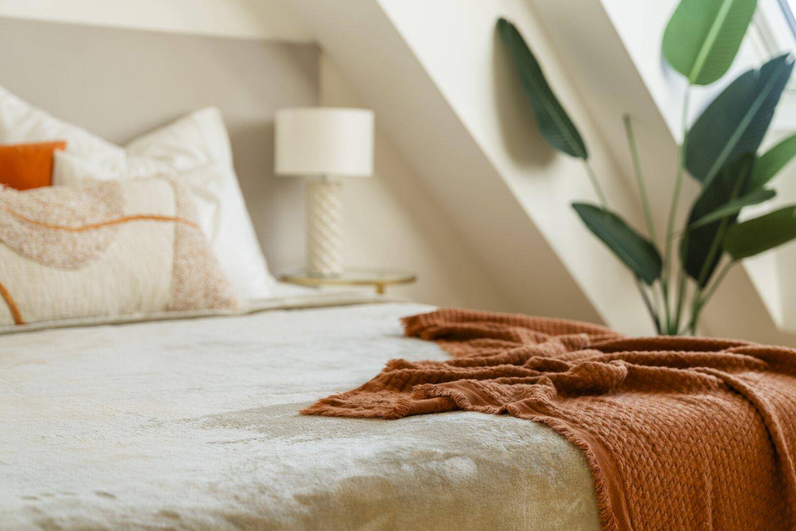 Gemütliches Schlafzimmer mit weicher Bettwäsche und einer warmen Decke unter der Dachschräge.