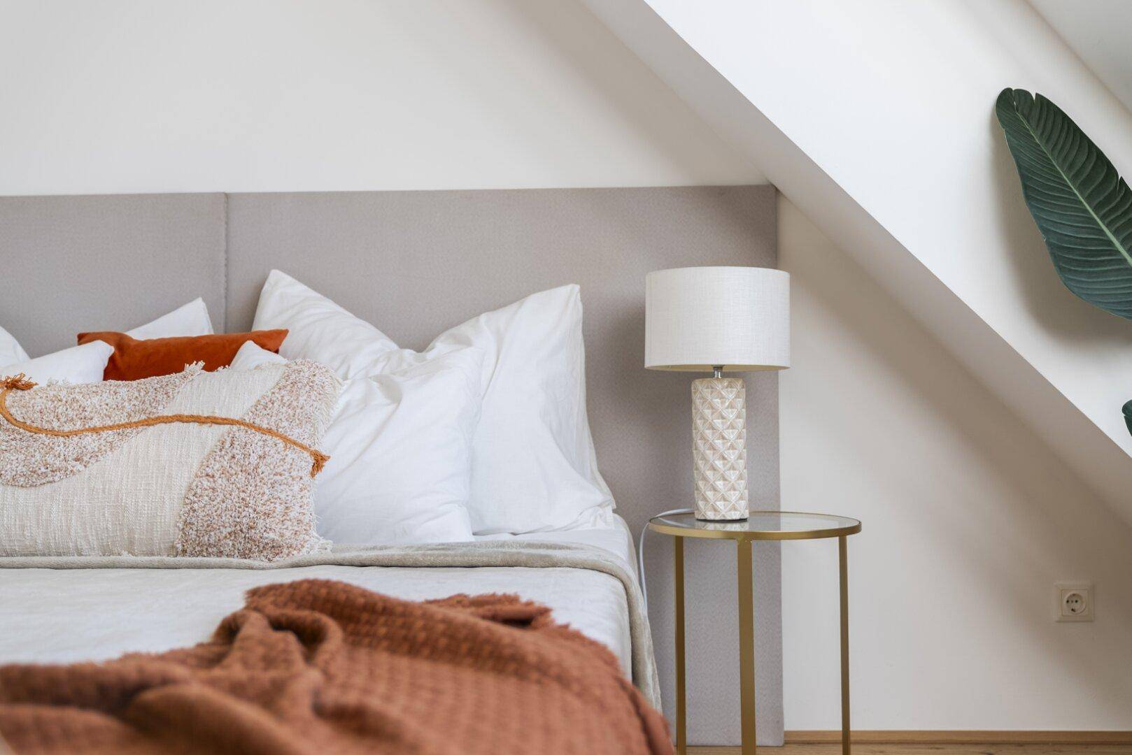 Nachttisch mit Lampe neben einem Bett in einem Schlafzimmer mit Dachschräge.