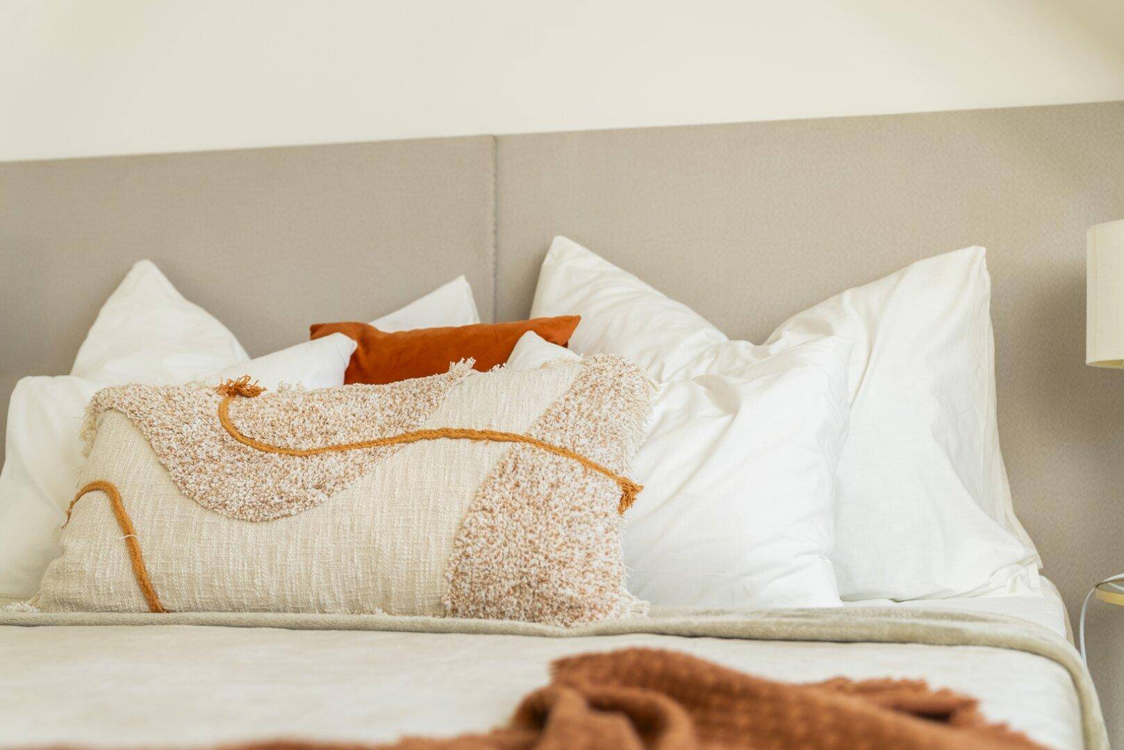 Nahaufnahme von Kissen und einer Decke auf einem Bett in einem hellen Schlafzimmer.