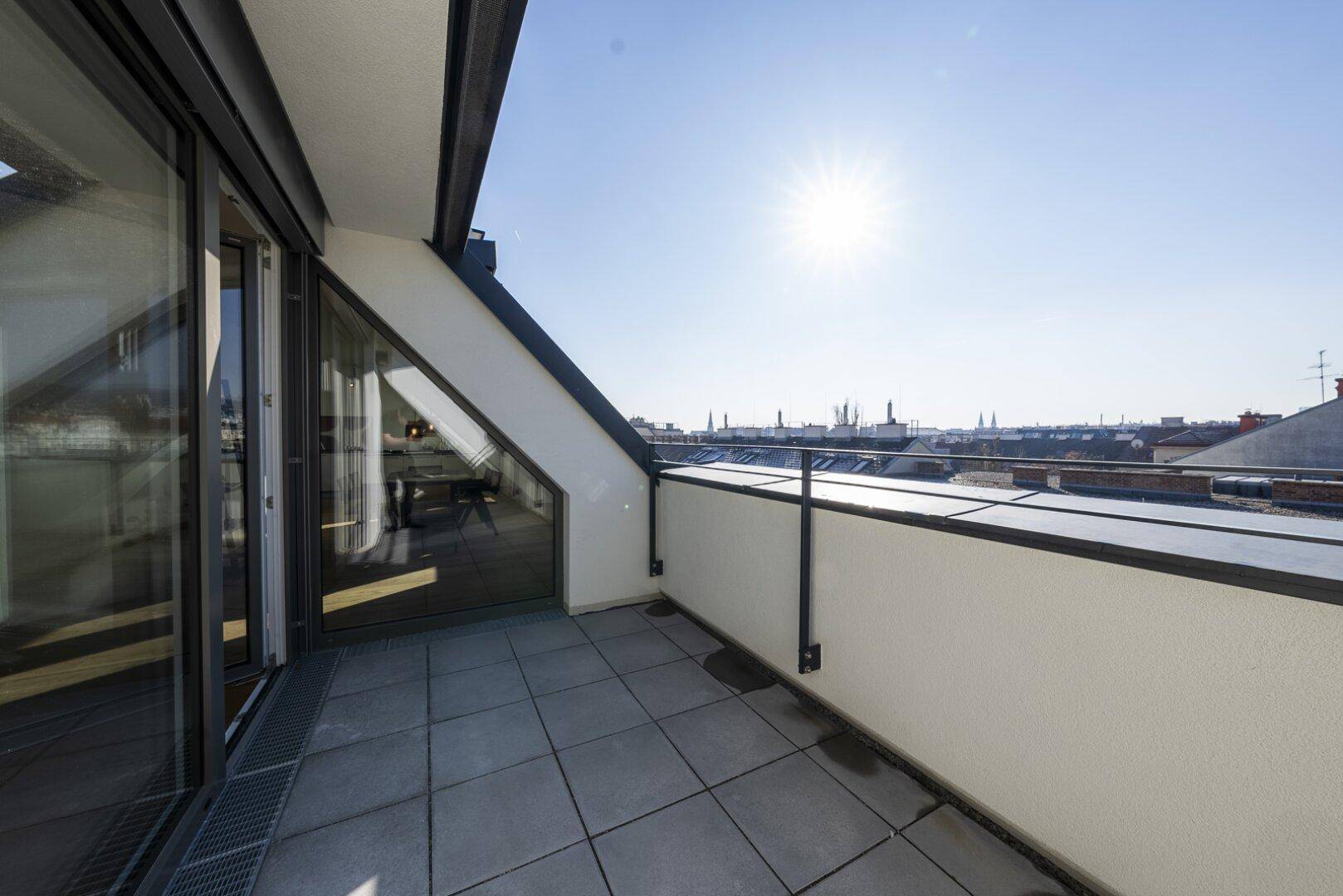 Sonnige Dachterrasse mit Fliesenboden und Blick auf die Dächer der Stadt.