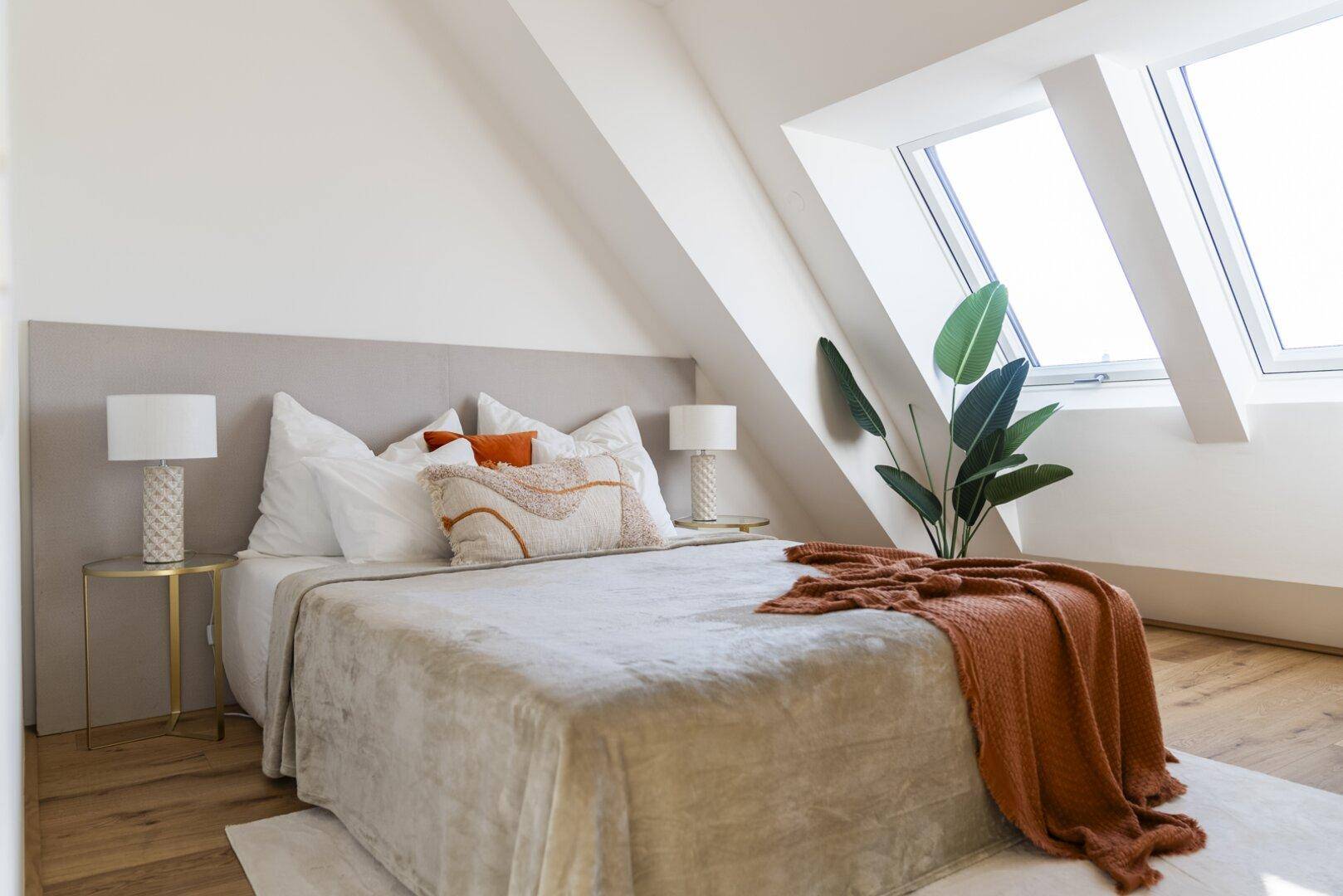 Helles Schlafzimmer im Dachgeschoss mit großem Bett, Dachfenstern und Holzboden.