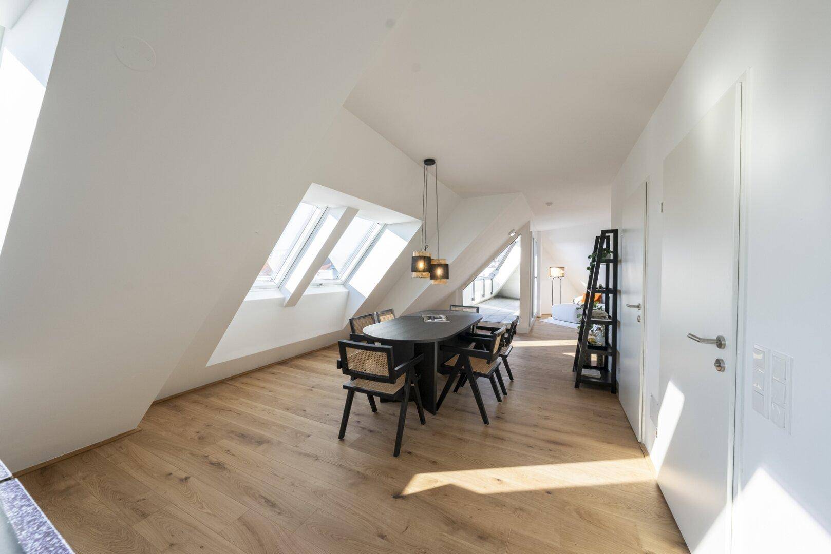 Eleganter Essbereich mit dunklem Tisch und Stühlen unter Dachfenstern und Holzboden.