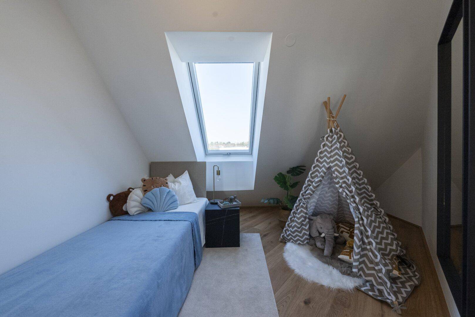 Helles Schlafzimmer im Dachgeschoss mit Einzelbett, Spielzelt und großem Dachfenster.