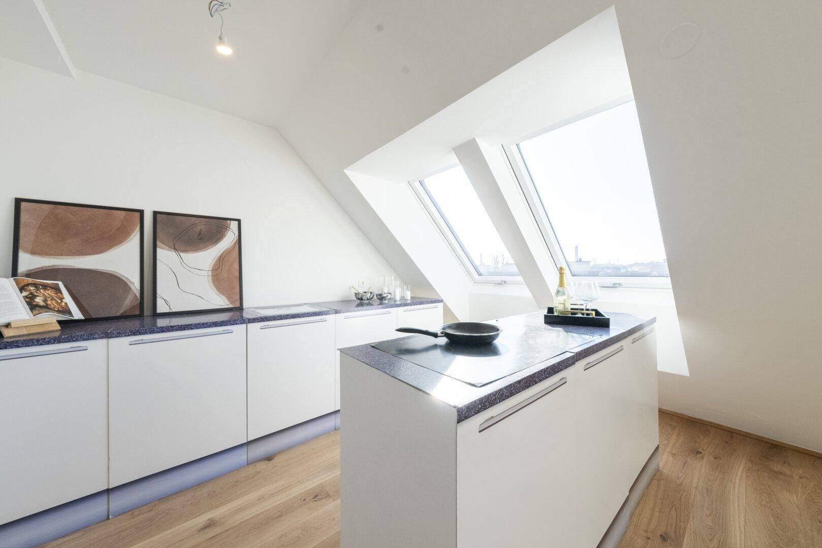Moderne Küche mit weißer Kücheninsel, blauen Arbeitsplatten und großen Dachfenstern.