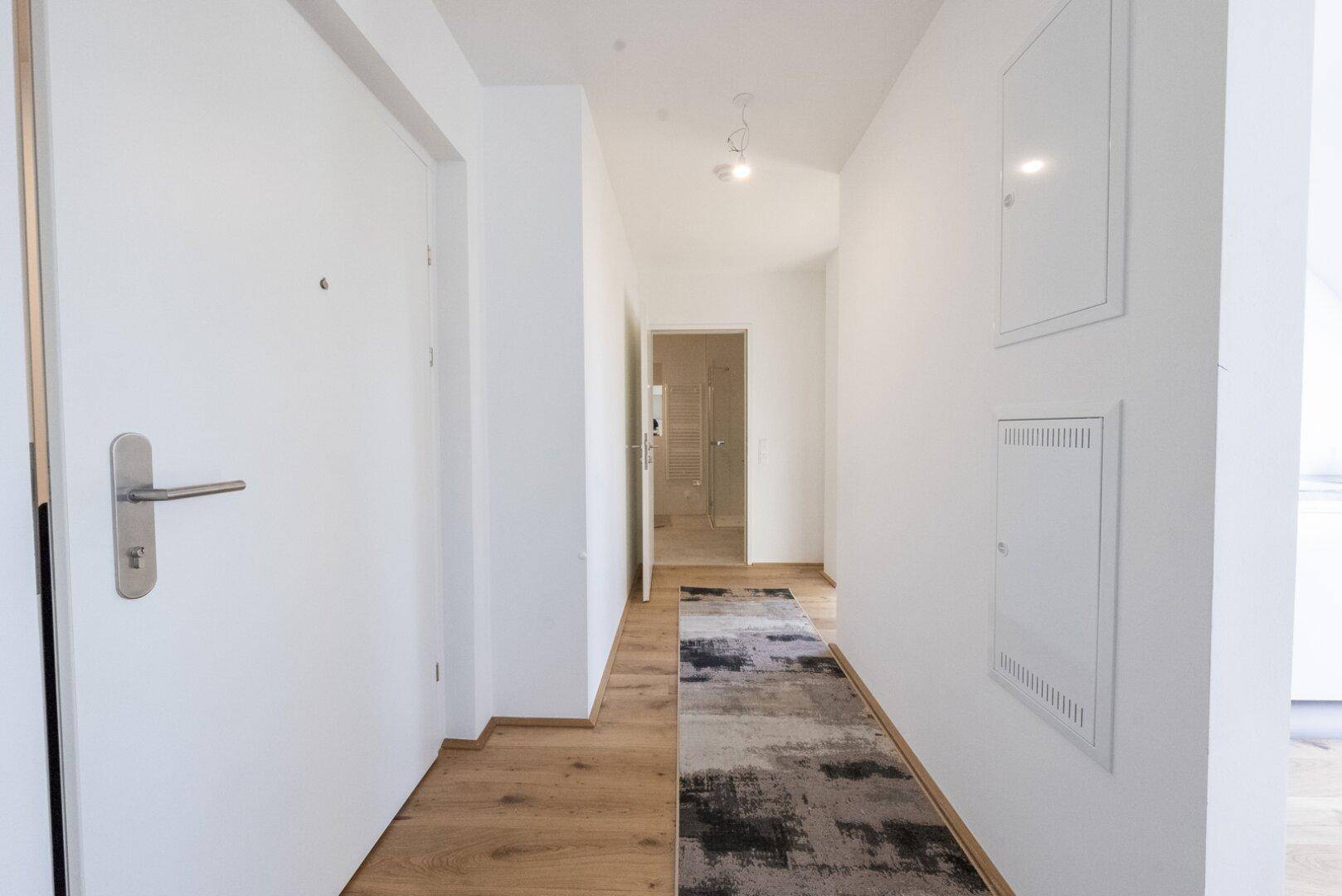 Heller Flur mit Holzboden, weiß gestrichenen Wänden und modernem Teppichläufer.