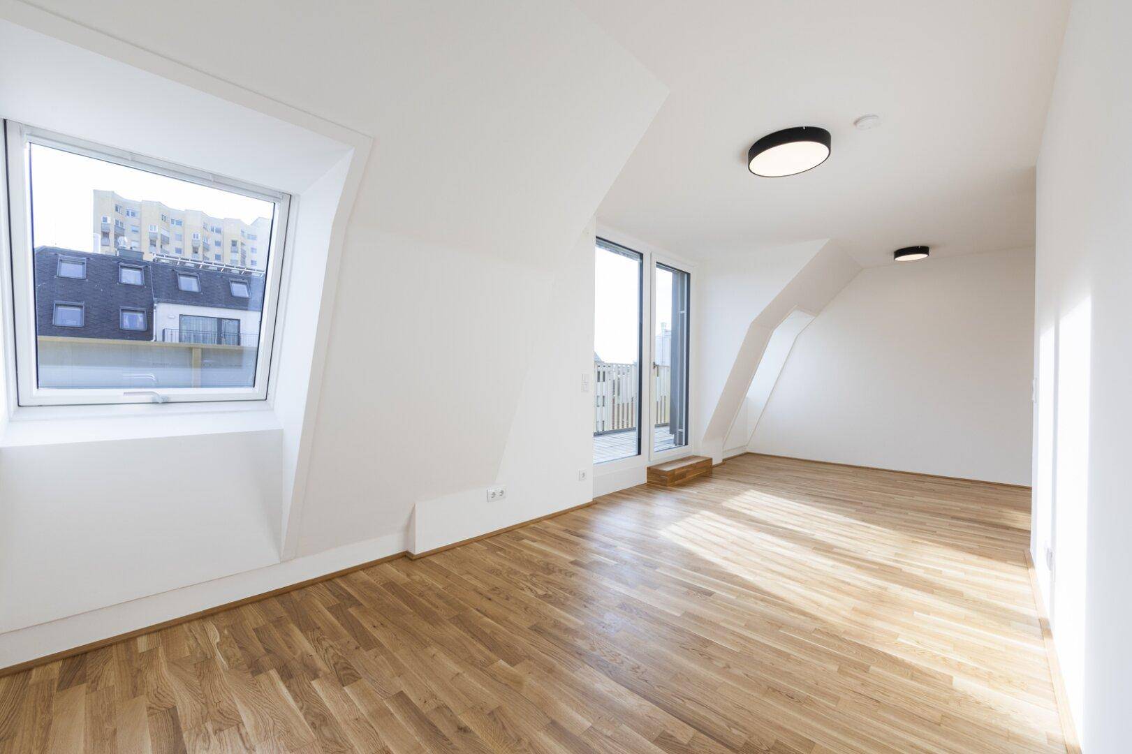 Geräumiges, helles Zimmer mit Parkettboden, Dachschrägen und Zugang zu einem Balkon oder einer Terrasse.