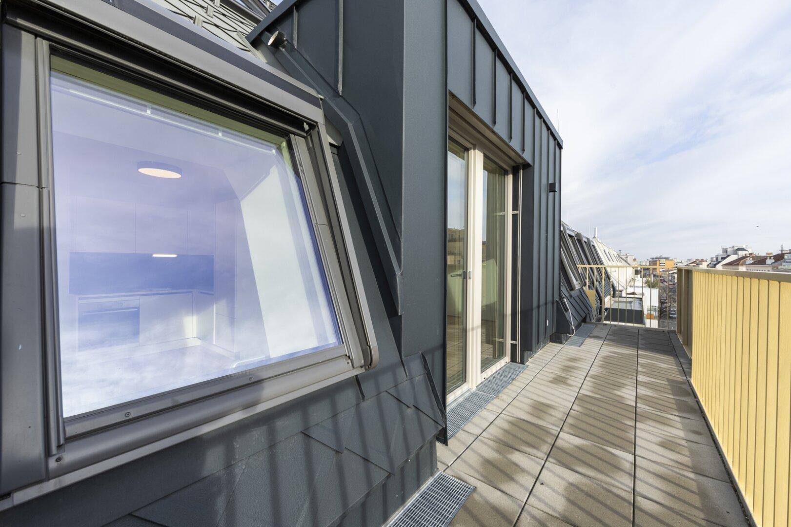 Dachterrasse mit Fliesenboden, Blick auf die Stadt und Zugang durch eine große Glastür.