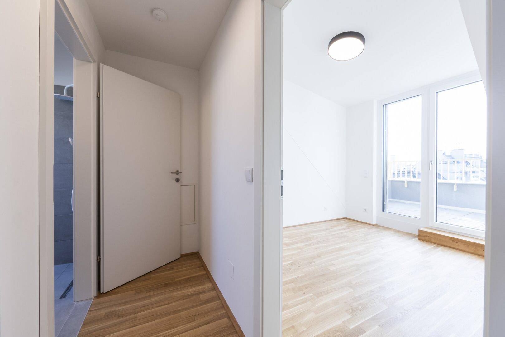 Heller Flur mit Holzparkett, der in einen Wohnbereich mit Balkonzugang führt.