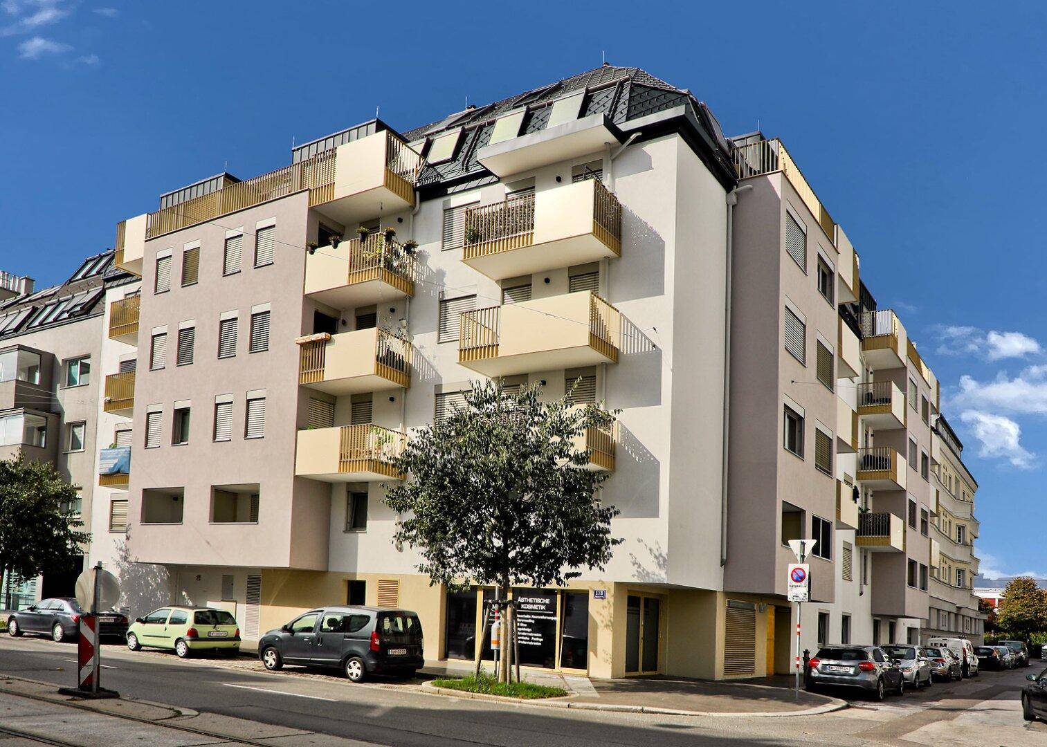 Modernes Mehrfamilienhaus mit Balkonen, Dachgeschosswohnungen und Geschäften im Erdgeschoss.