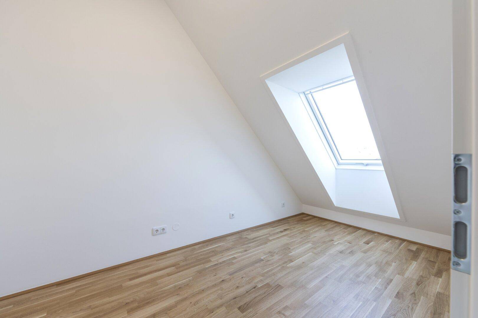 Helles Zimmer im Dachgeschoss mit Holzboden und einem großen Dachfenster.