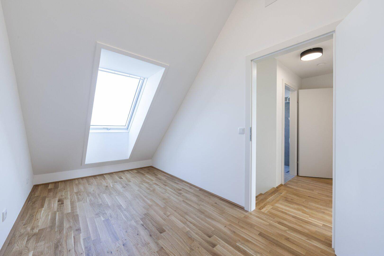 Helles Schlafzimmer im Dachgeschoss mit Holzparkett und großem Dachfenster.