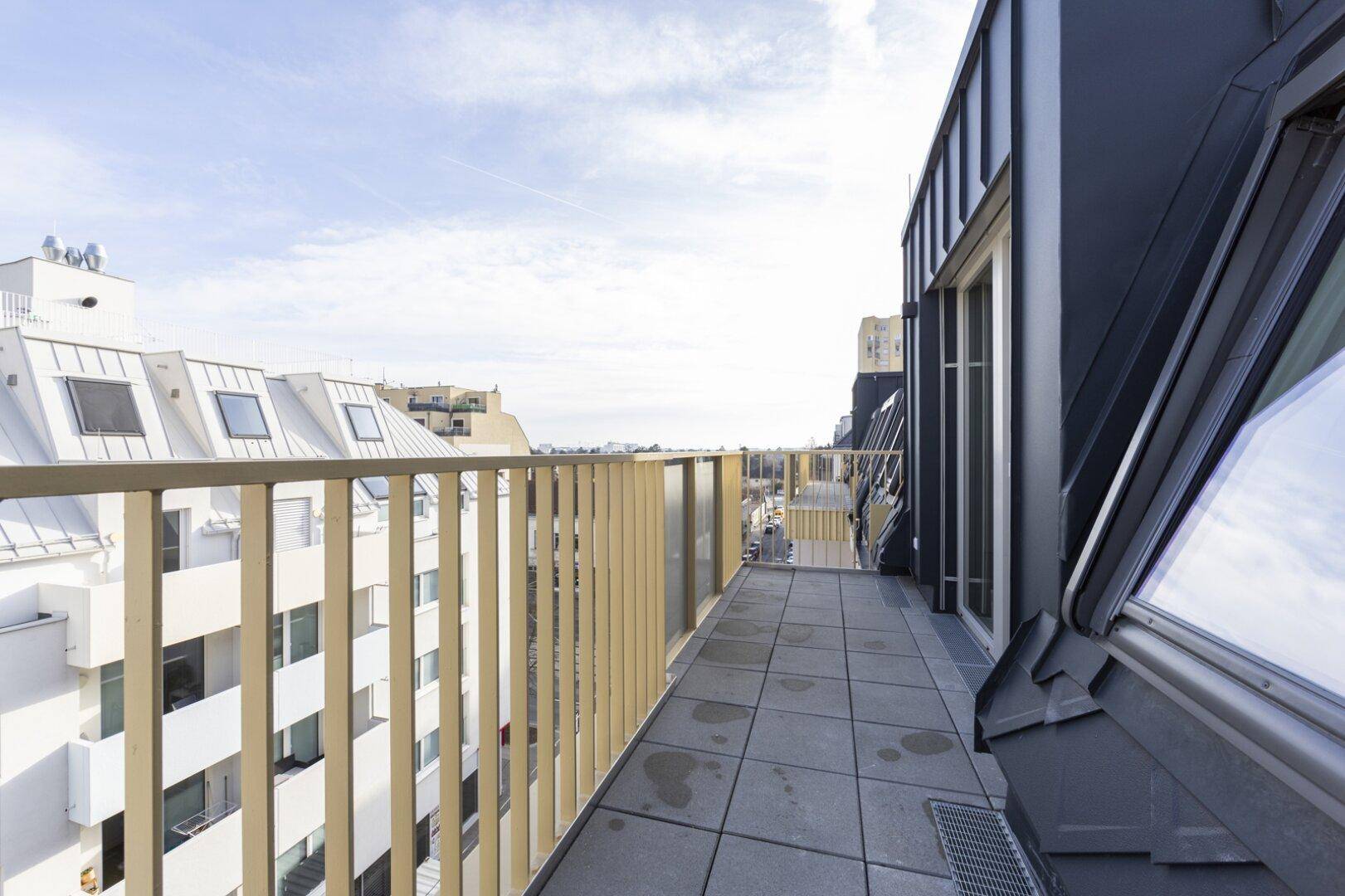 Schmaler Balkon mit Fliesenboden, modernem Geländer und Blick über die Dächer der Stadt.