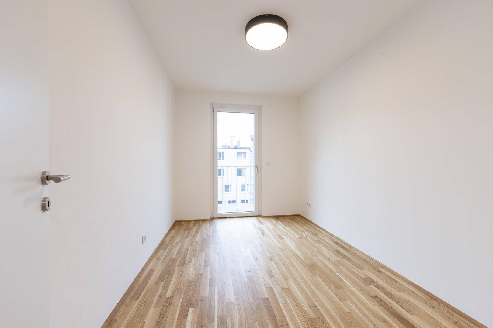 Helles Schlafzimmer mit Parkettboden und direktem Zugang zu einem kleinen Balkon.