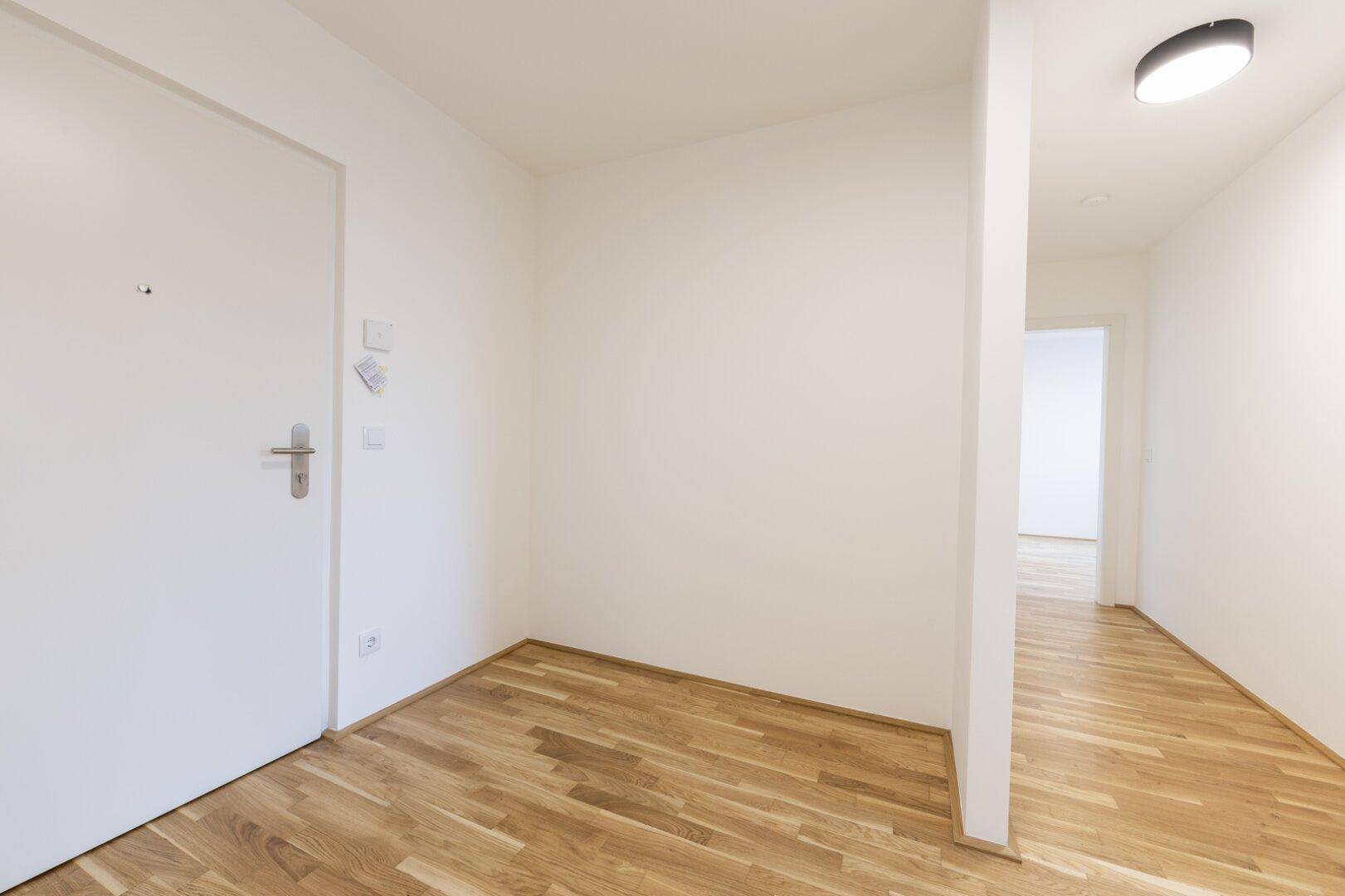 Eingangsbereich mit weißer Wohnungstür und Parkettboden, der in einen hellen Flur übergeht.