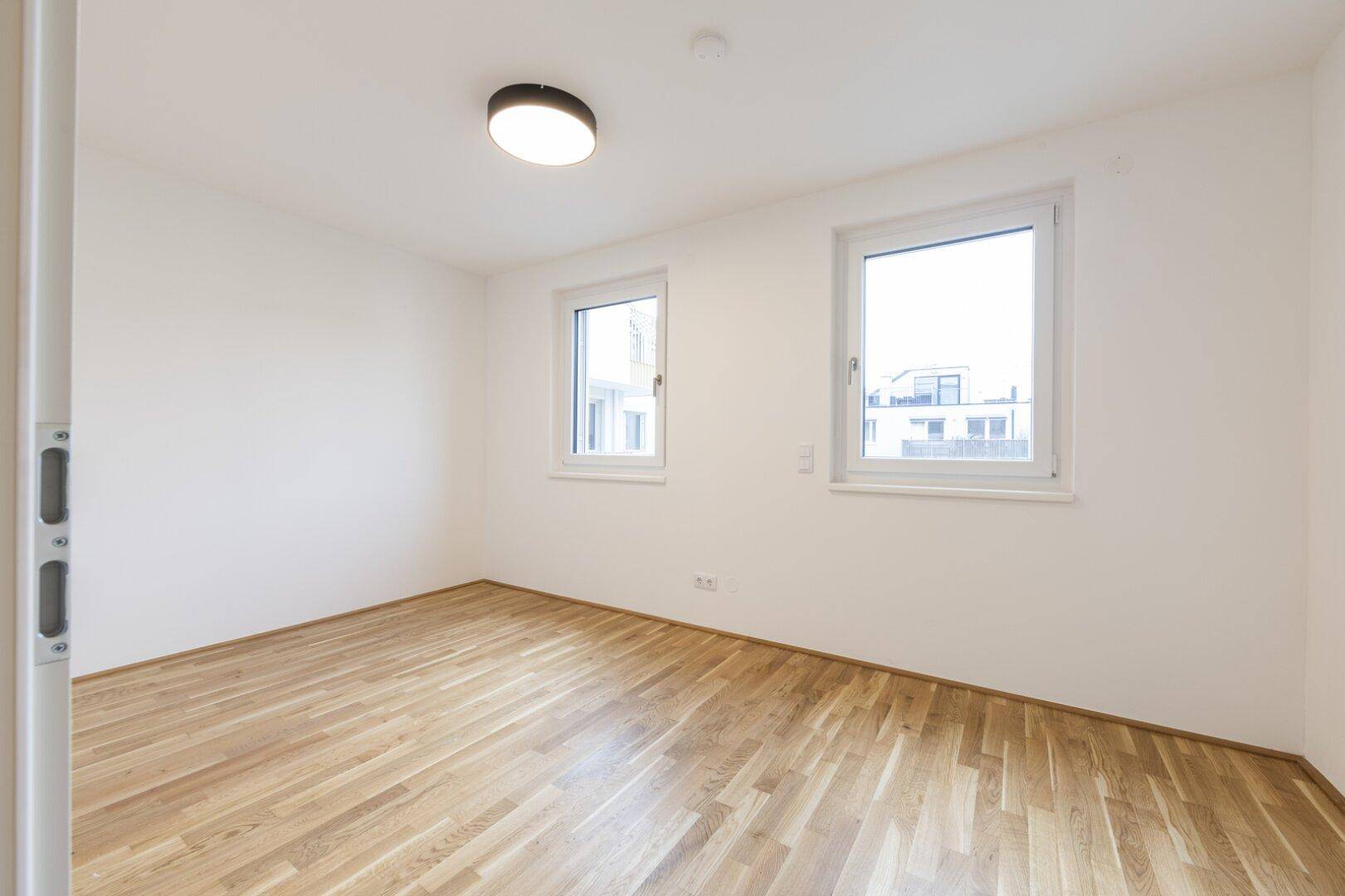 Helles Zimmer mit Parkettboden und zwei Fenstern, ideal als Schlaf- oder Kinderzimmer.
