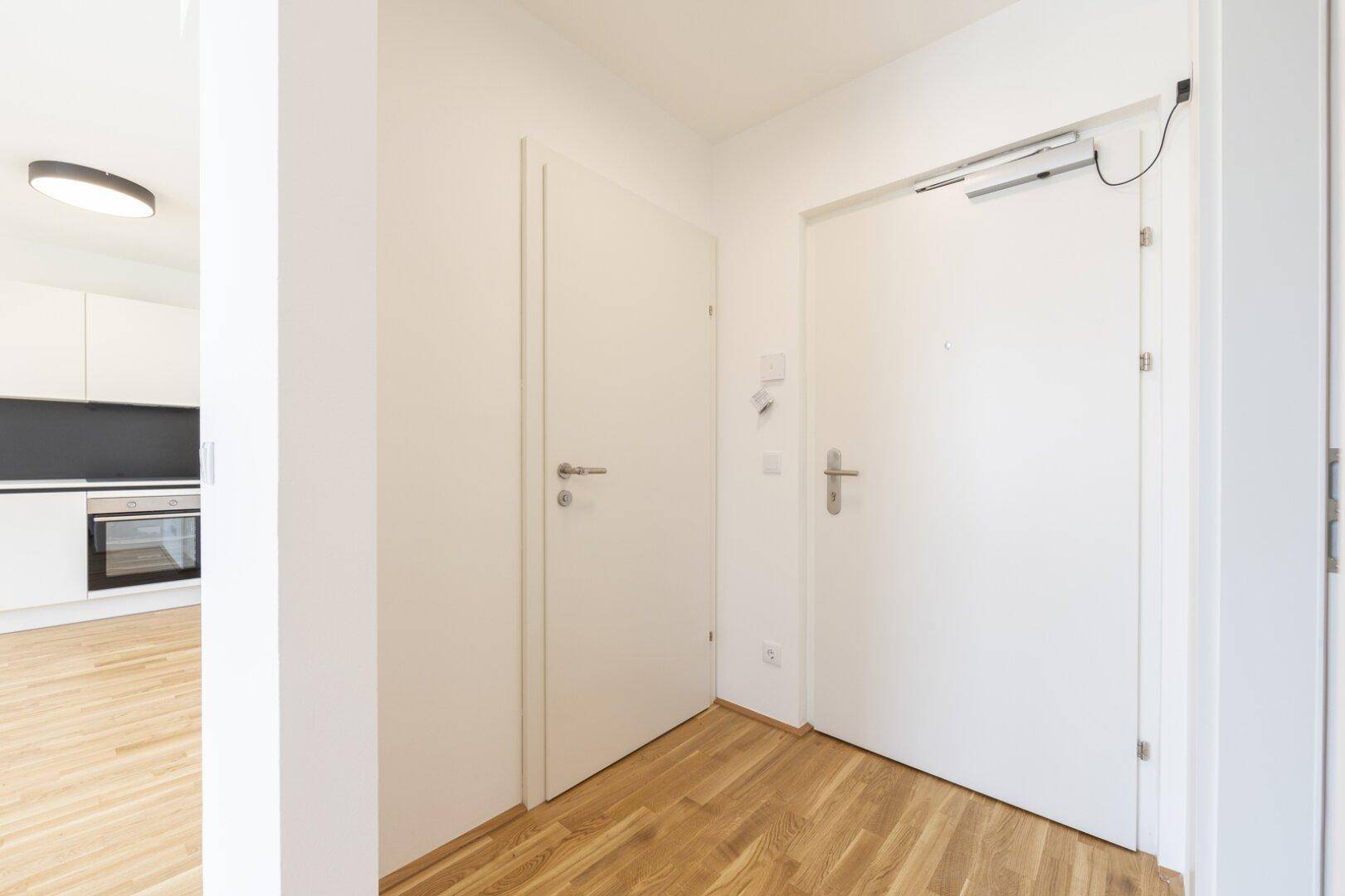 Heller Eingangsbereich mit Holzboden und weißen Türen, angrenzend an den offenen Wohnbereich.