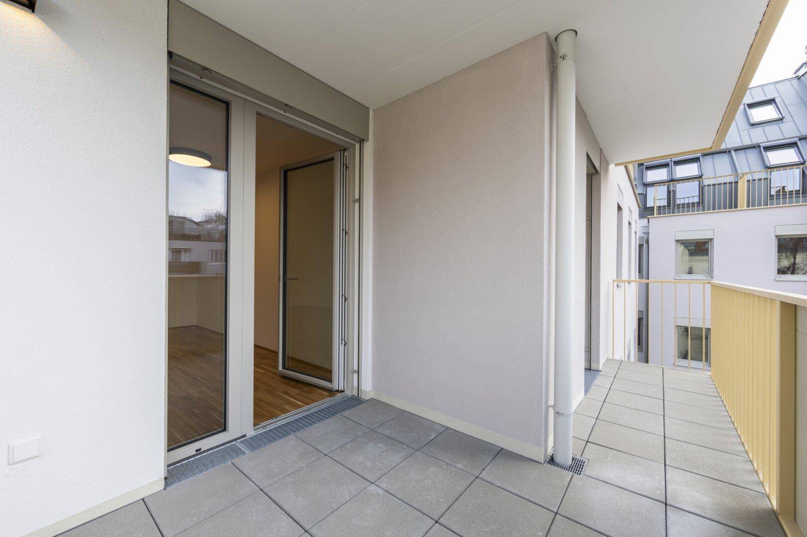 Heller Balkon mit Fliesenboden und gelbem Geländer, mit Blick auf die umliegenden Gebäude.