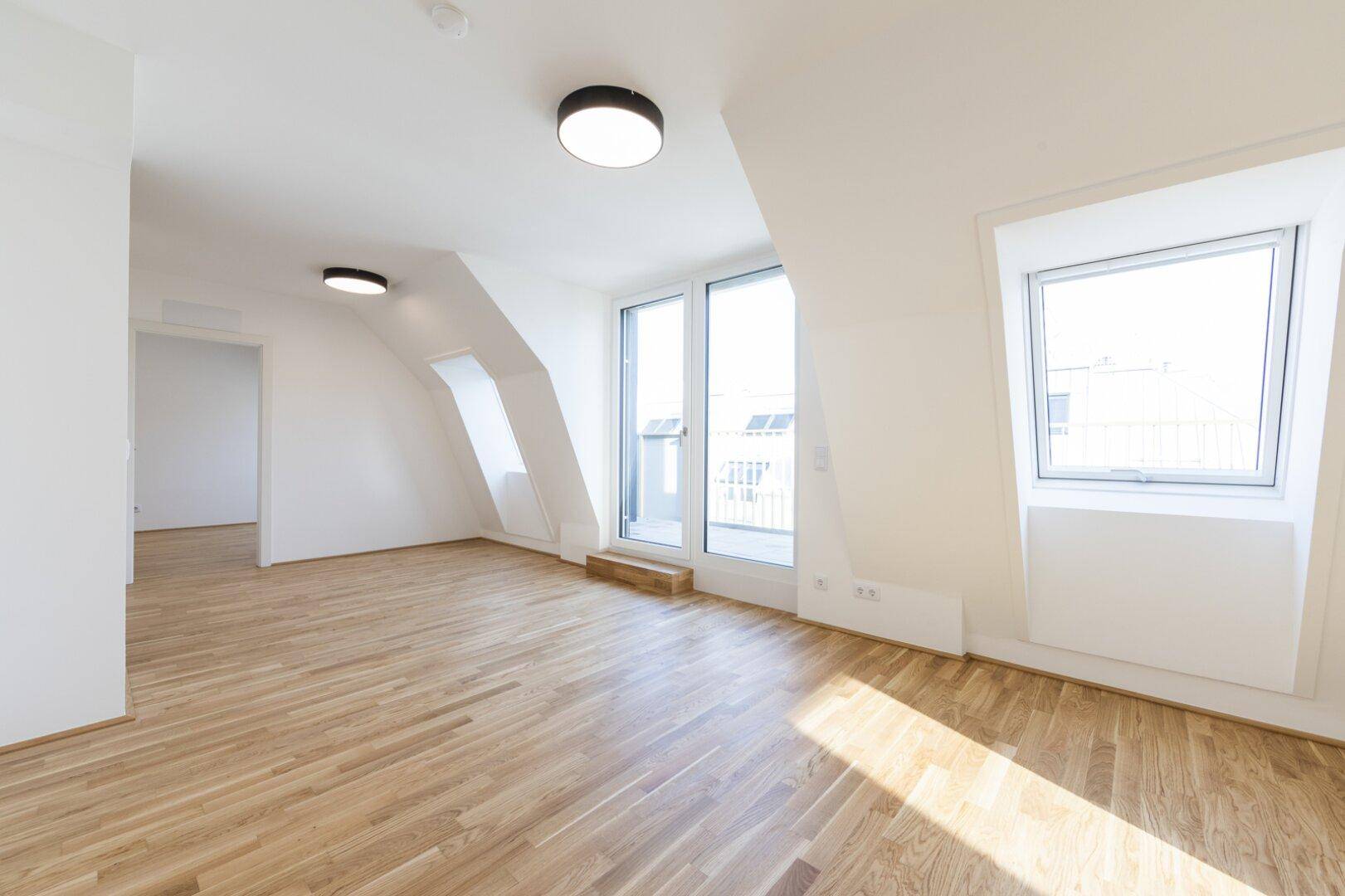 Lichtdurchfluteter Wohnbereich im Dachgeschoss mit großen Fenstern und Zugang zur Terrasse.